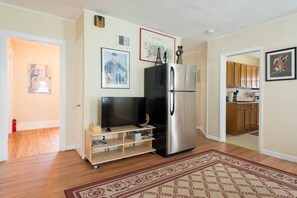 A compact kitchen with a refrigerator, a television on a stand, and a wooden cabinet.