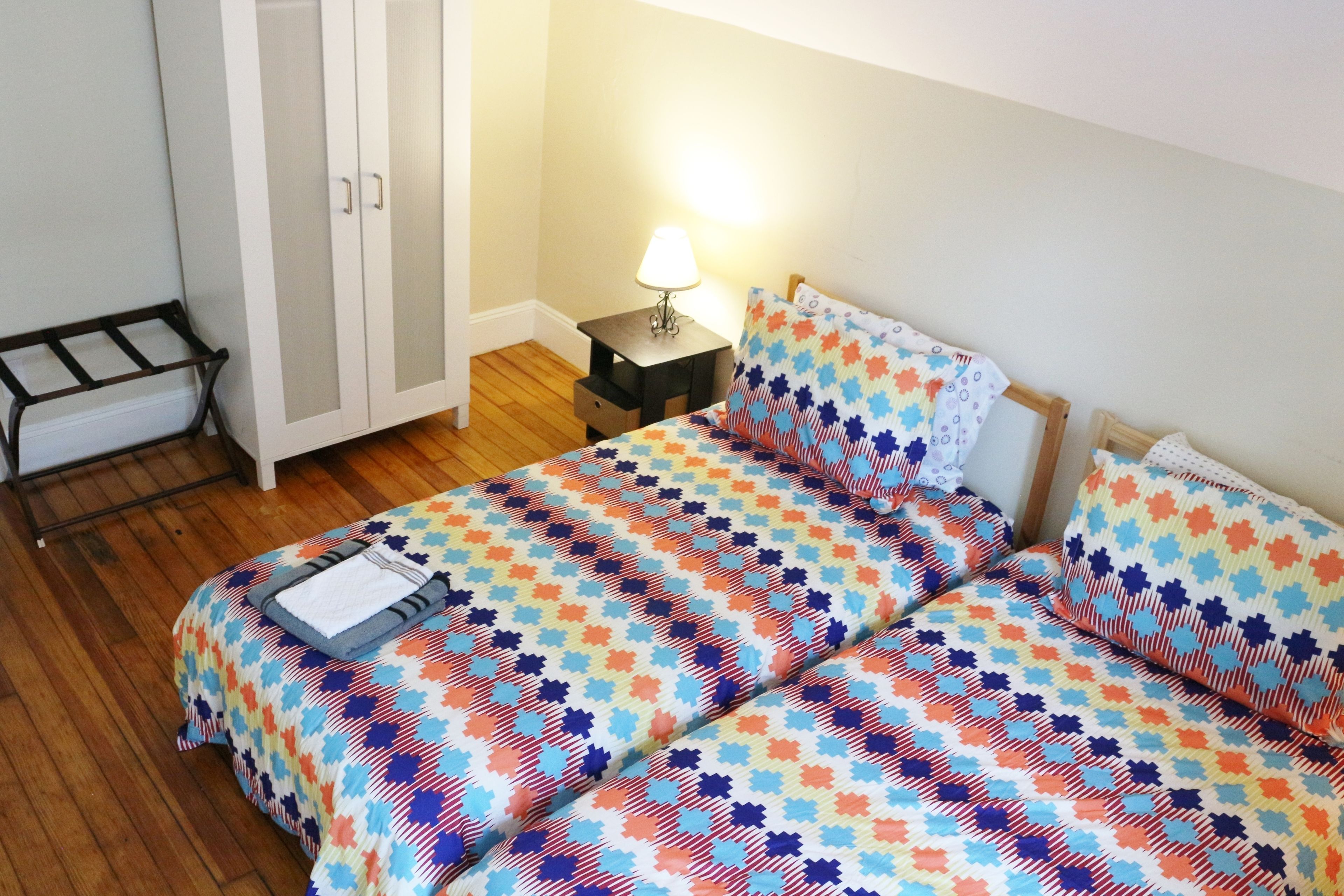 A bedroom with a bed, a nightstand, a lamp, and a wardrobe.