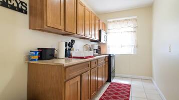 A compact kitchen with wooden cabinets, a microwave, a coffee maker, and a red patterned rug.