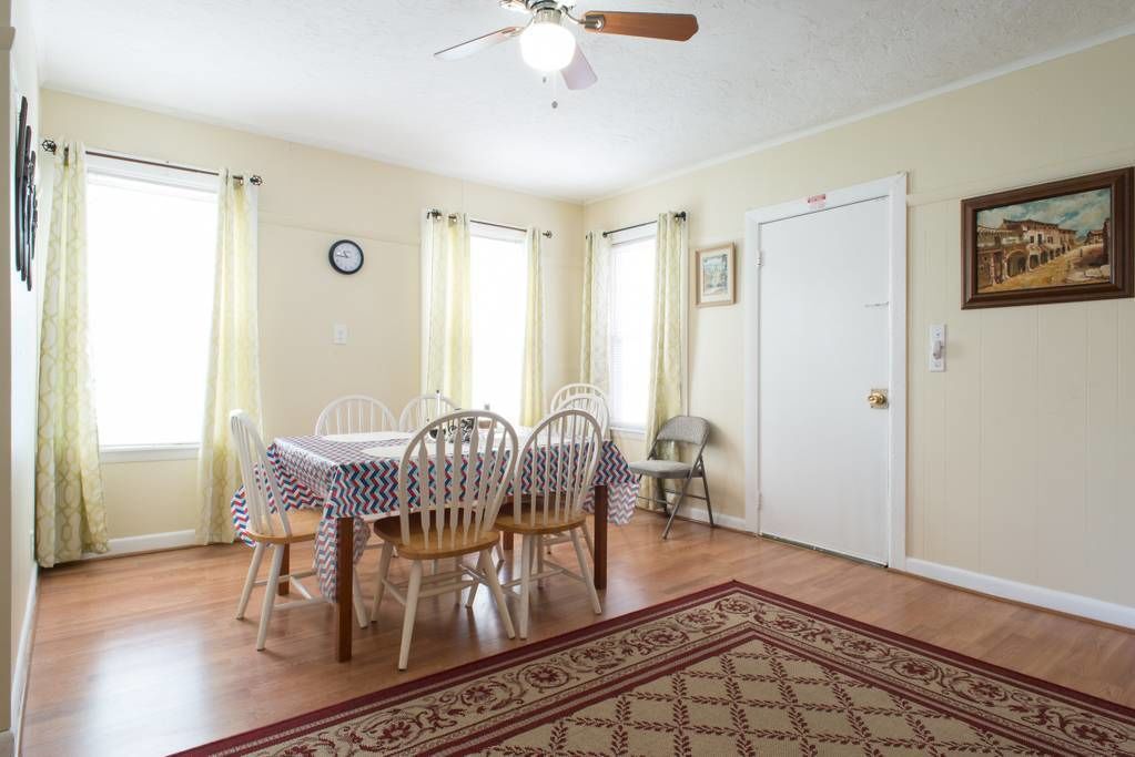 A dining room with a table set for four, a ceiling fan, and a door with a picture frame.