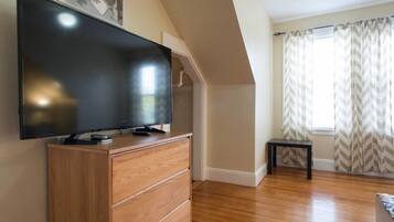 Una habitación con una televisión de pantalla plana sobre un tocador de madera, una mesita y una ventana con cortinas a cuadros.