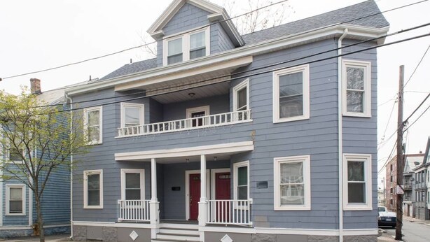 A two-story house with a front porch, a red door, and a small balcony.