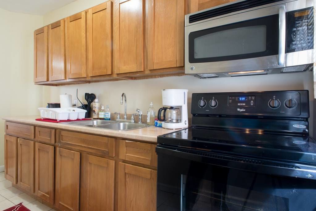 A kitchen with wooden cabinets, a stainless steel microwave, a black stove, and a coffee maker.