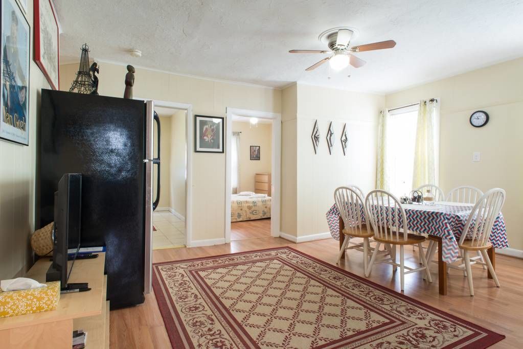 A dining area with a table set for four, a ceiling fan, and a patterned rug.