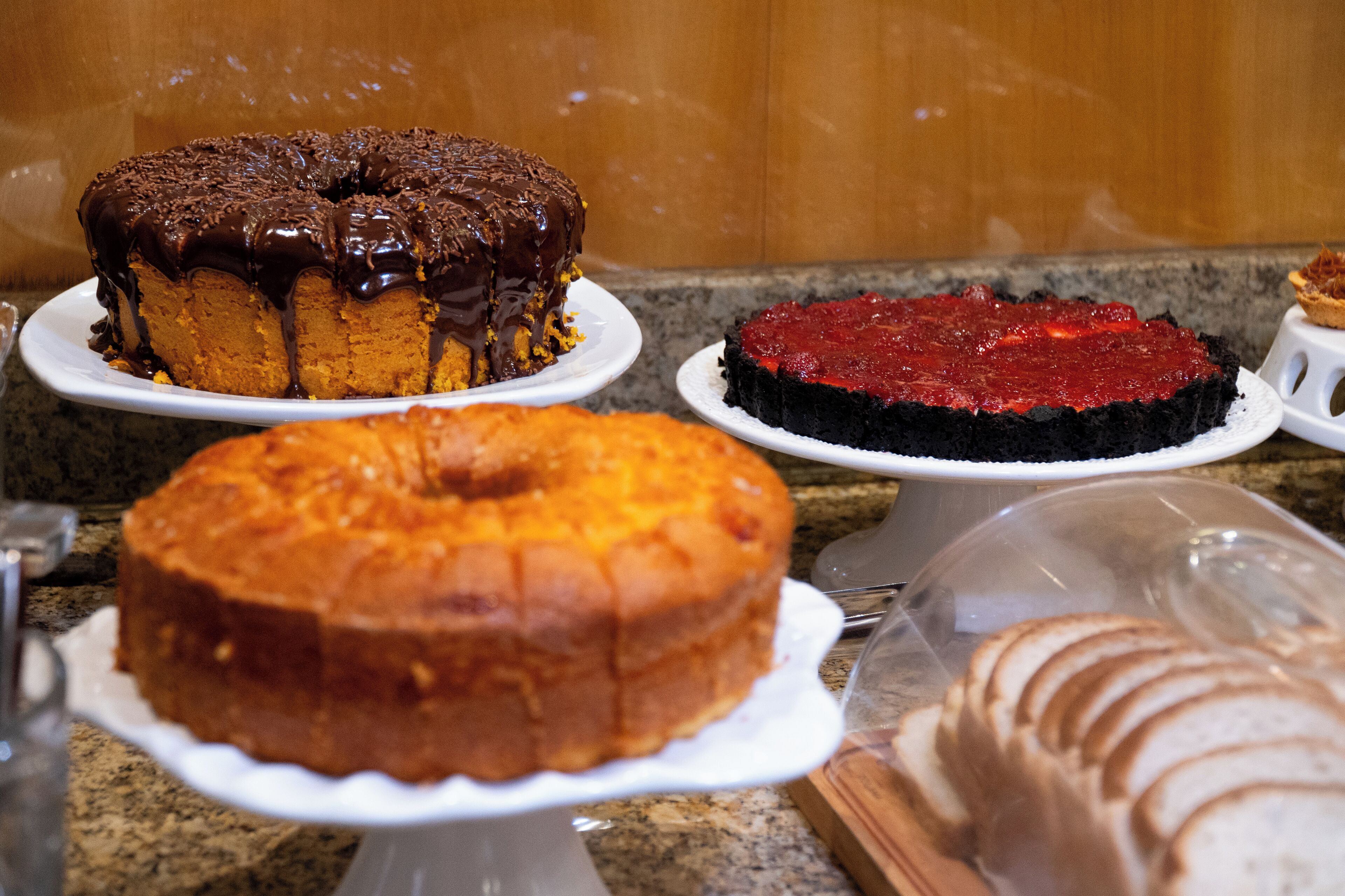 Una selezione di torte in mostra, tra cui una torta al cioccolato con glassa lucida e una torta rossa dalla superficie liscia.