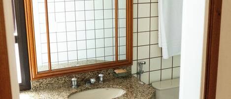 A bathroom with a wooden-framed mirror, a granite countertop sink, a white toilet, and a metal trash can.
