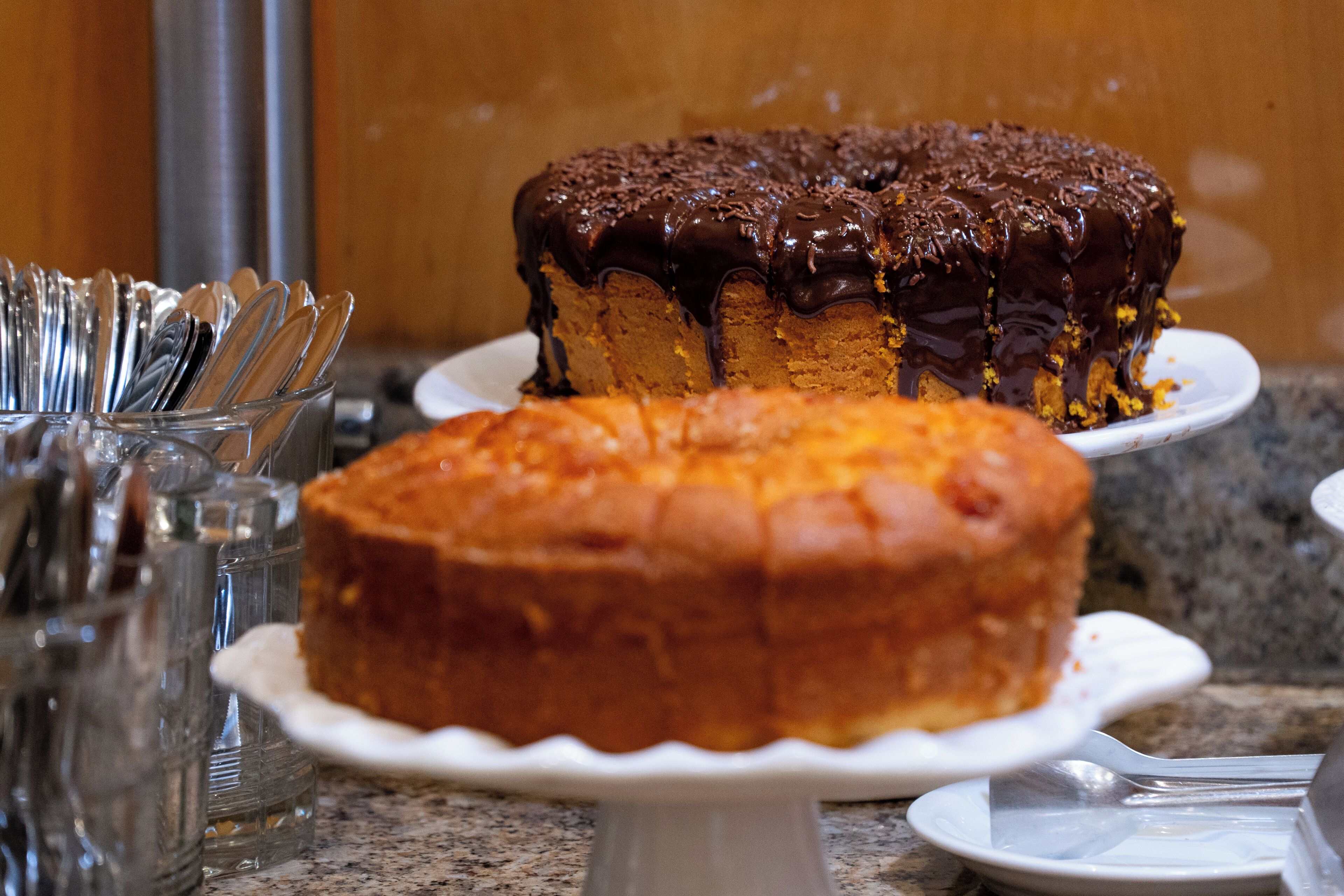 Una encimera de cocina con dos pasteles en platos blancos, un recipiente de vidrio con utensilios, y un electrodoméstico de acero inoxidable al fondo.