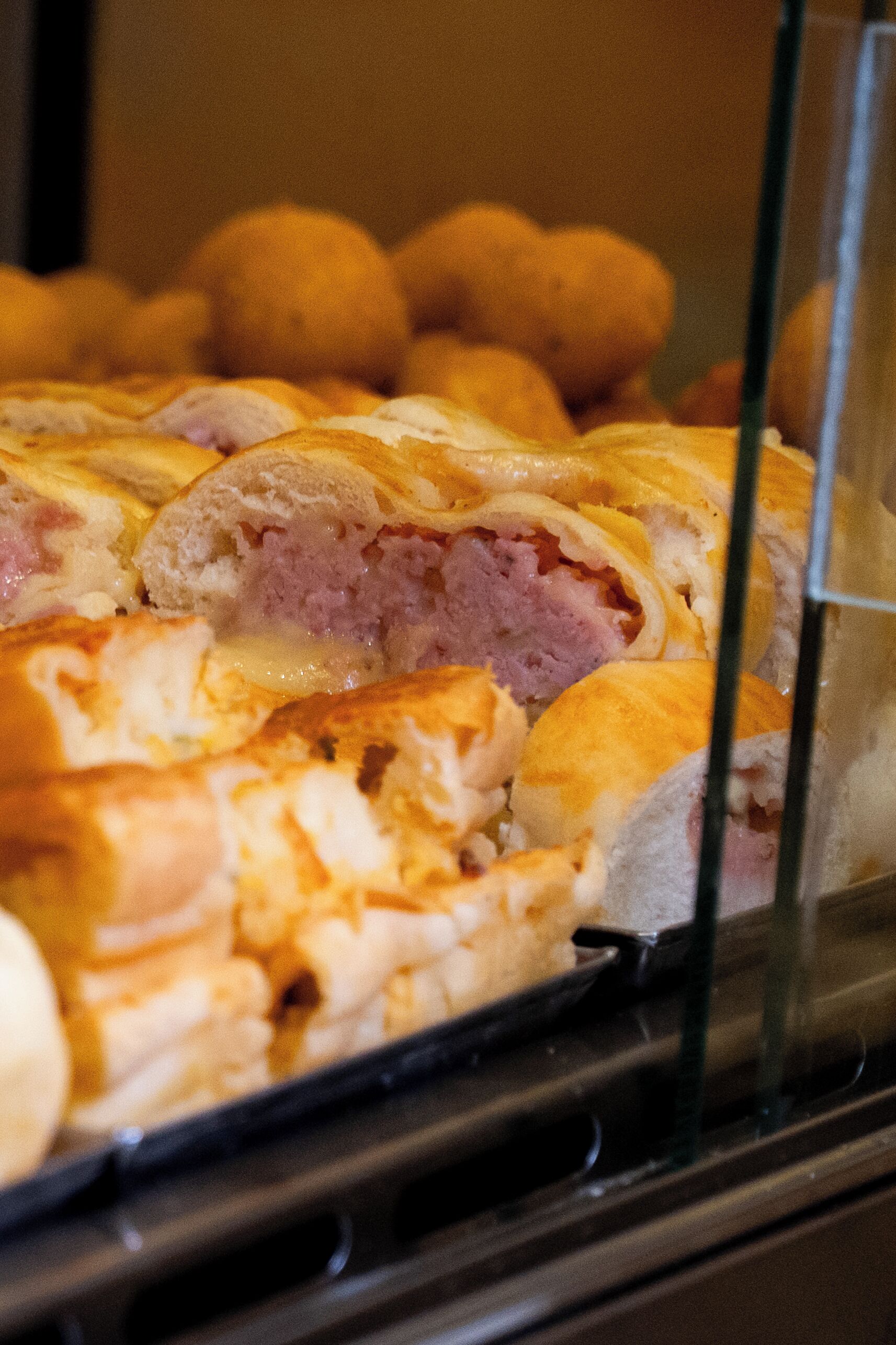 A display case containing various baked goods, likely pastries or bread rolls, with visible fillings.