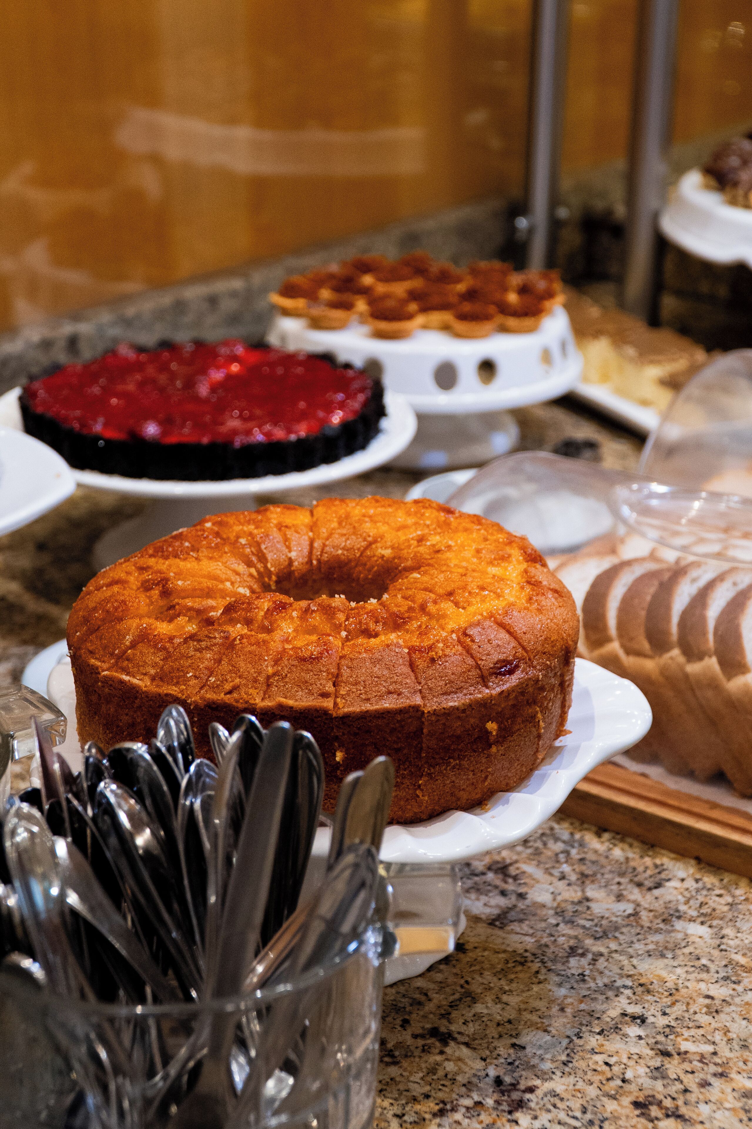 A variety of cakes on display, including a bundt cake and a red velvet cake, on a marble countertop.