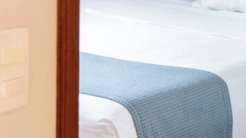Una habitación de hotel con cama, ropa de cama blanca y cabecero de madera.
