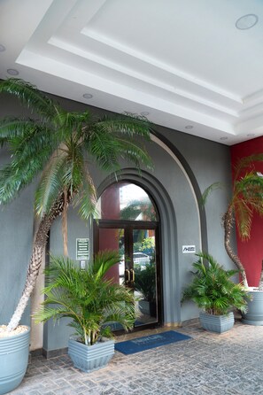 A hotel entrance with a modern design, featuring a large arched doorway, potted palm trees, and a blue mat at the entrance. - New Life Piracicaba by Atlantica (Piracicaba)
