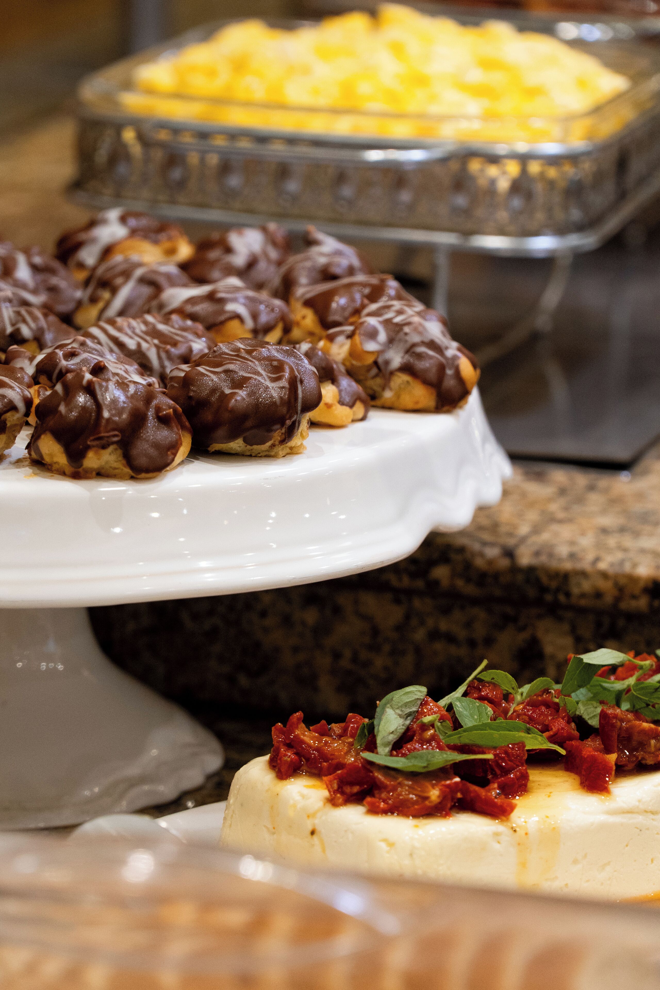 Un bufé con diversos platos, incluyendo un preparado de queso blanco cubierto de salsa roja y nueces, y una bandeja de pasteles bañados en chocolate.