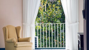 A room with a beige armchair, a balcony with a white railing, and a view of greenery. - Home47 (Salerno)
