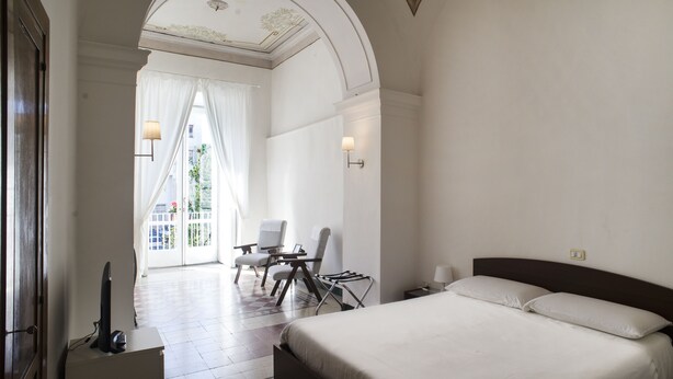 A hotel room with a large bed, a desk with a chair, a TV, and a view of a balcony with curtains. - Home47 (Salerno)
