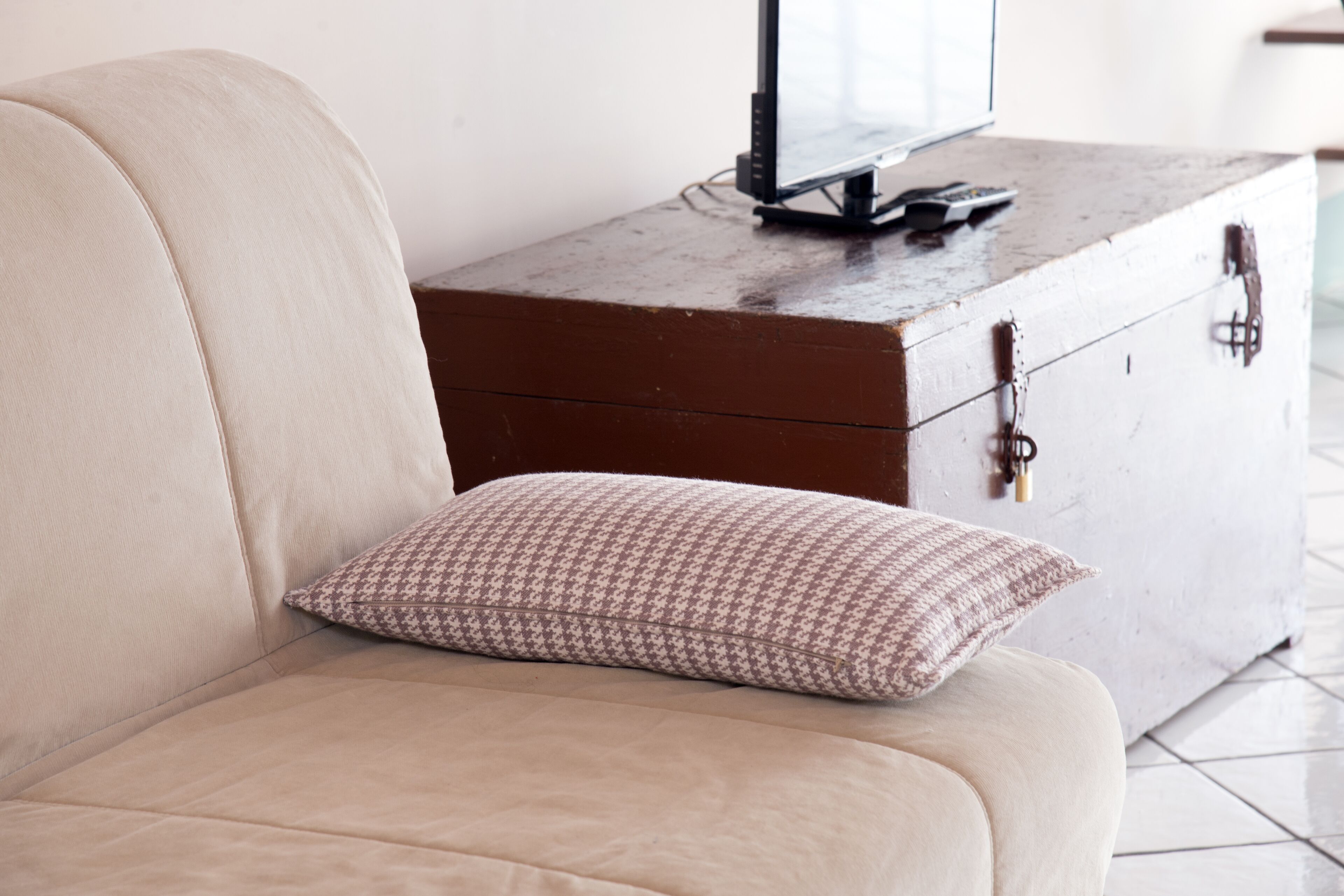 A beige sofa with a patterned pillow, a wooden dresser with a TV and remote, and a keychain.