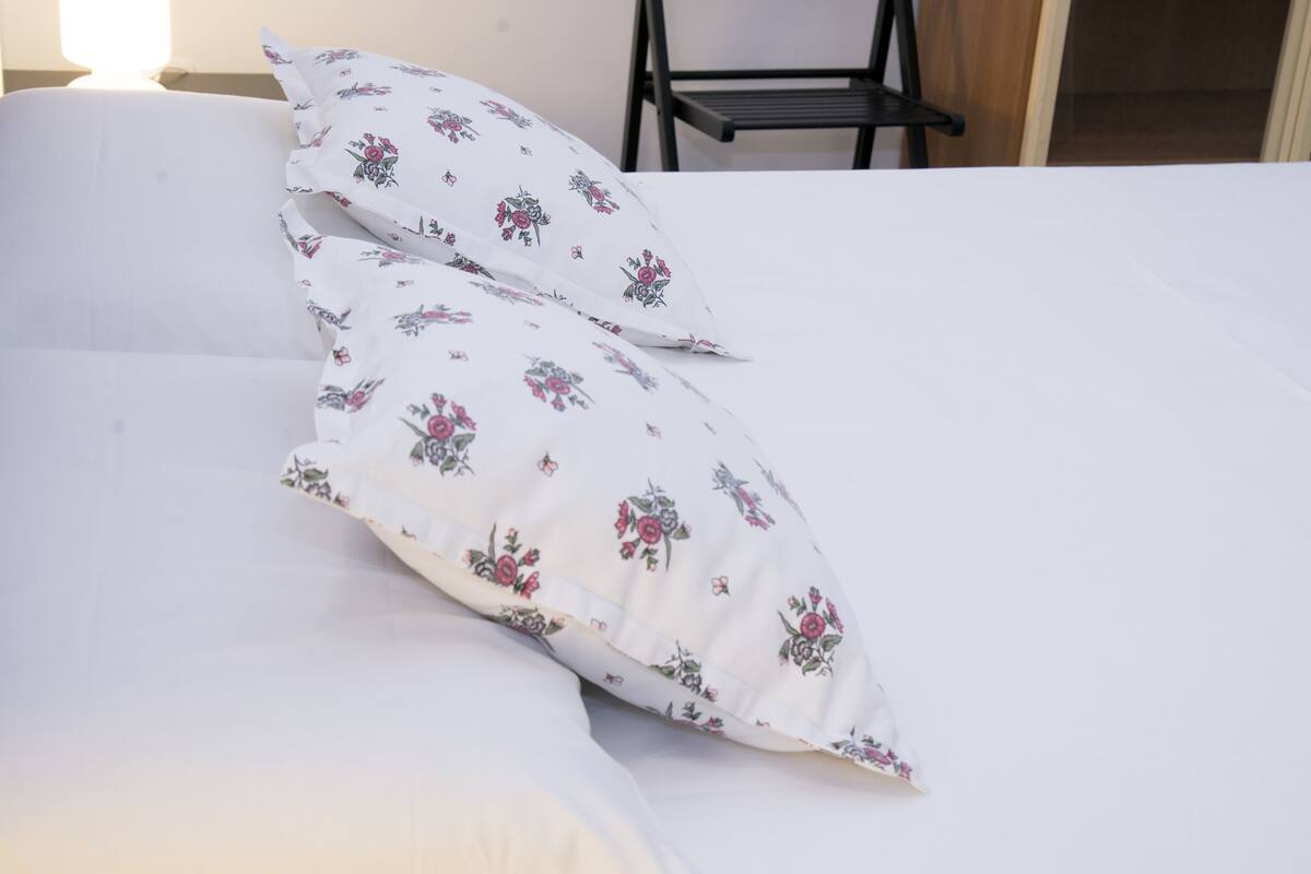 A bed with white bedding and floral-patterned pillows.