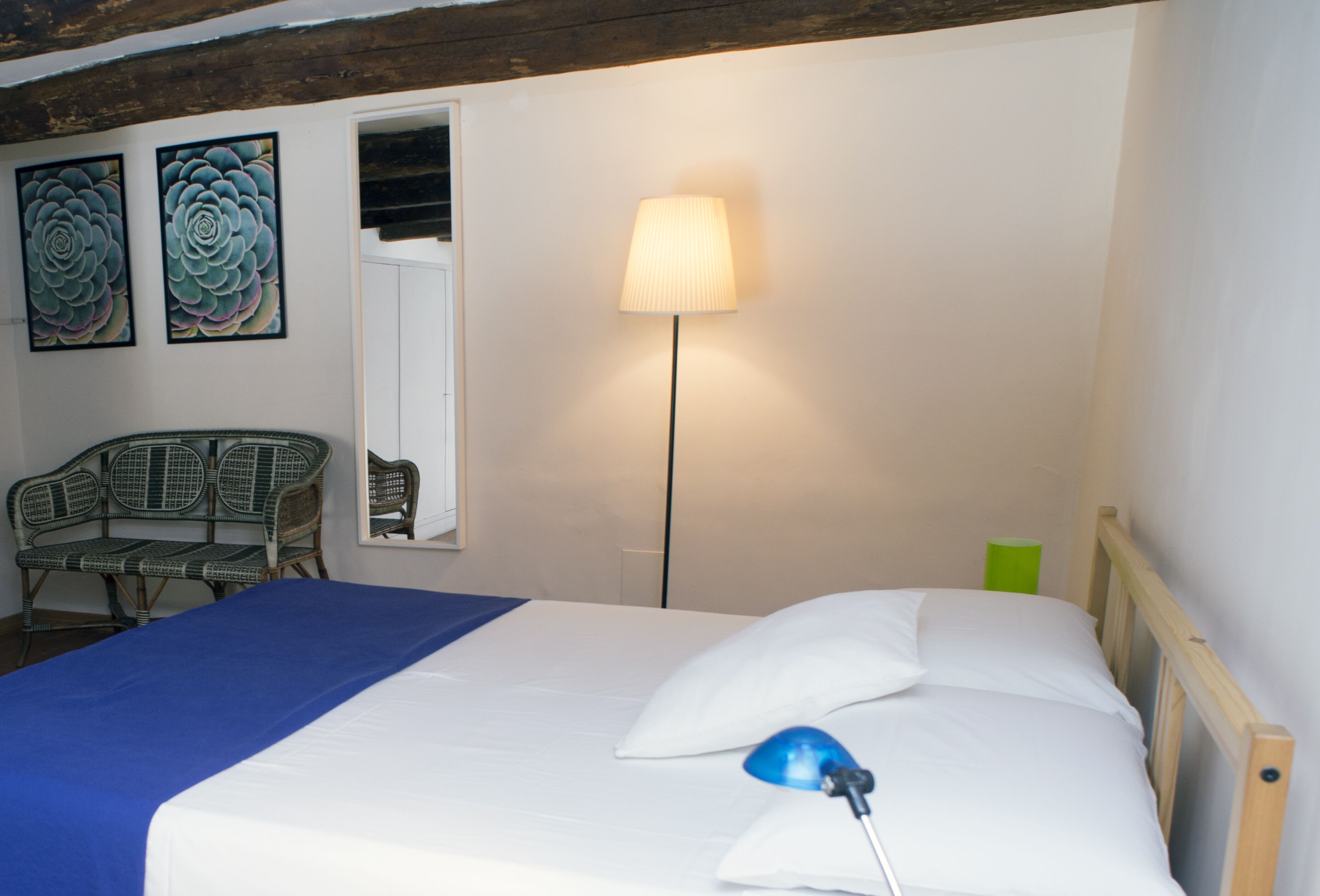 A bedroom with a bed, a lamp, a chair, and two wall art pieces.