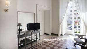 A hotel room with a desk, chair, TV, and a view of the outside. - Home47 (Salerno)