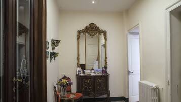 Un couloir avec une porte en bois, un miroir, une petite table sur laquelle est posé un vase de fleurs et un radiateur.