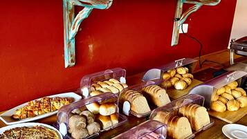 Buffet com diversos alimentos, incluindo doces, pães e uma torta.