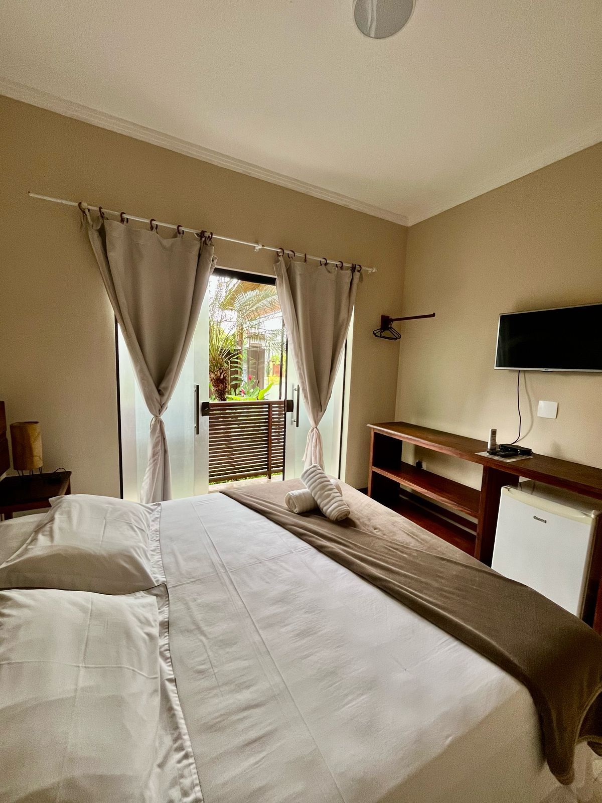 A hotel room with a bed, a television, a desk, and a view of the outdoors.