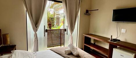 A hotel room with a bed, a television, a desk, and a view of the outdoors.