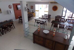 A spacious dining area with multiple wooden tables and chairs, a glass-top dining table, and a brick accent wall.
