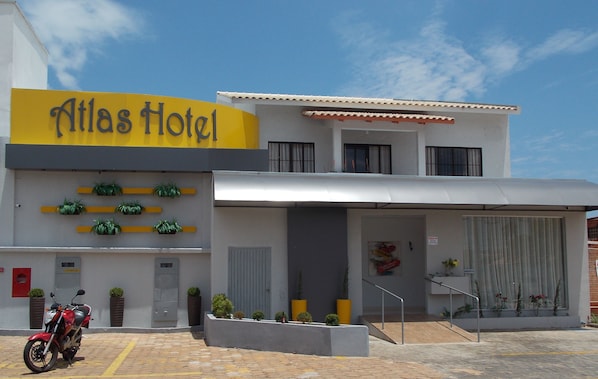 A modern hotel named Atlas Hotel with a yellow sign, a motorbike parked in front, and a staircase leading to the entrance.