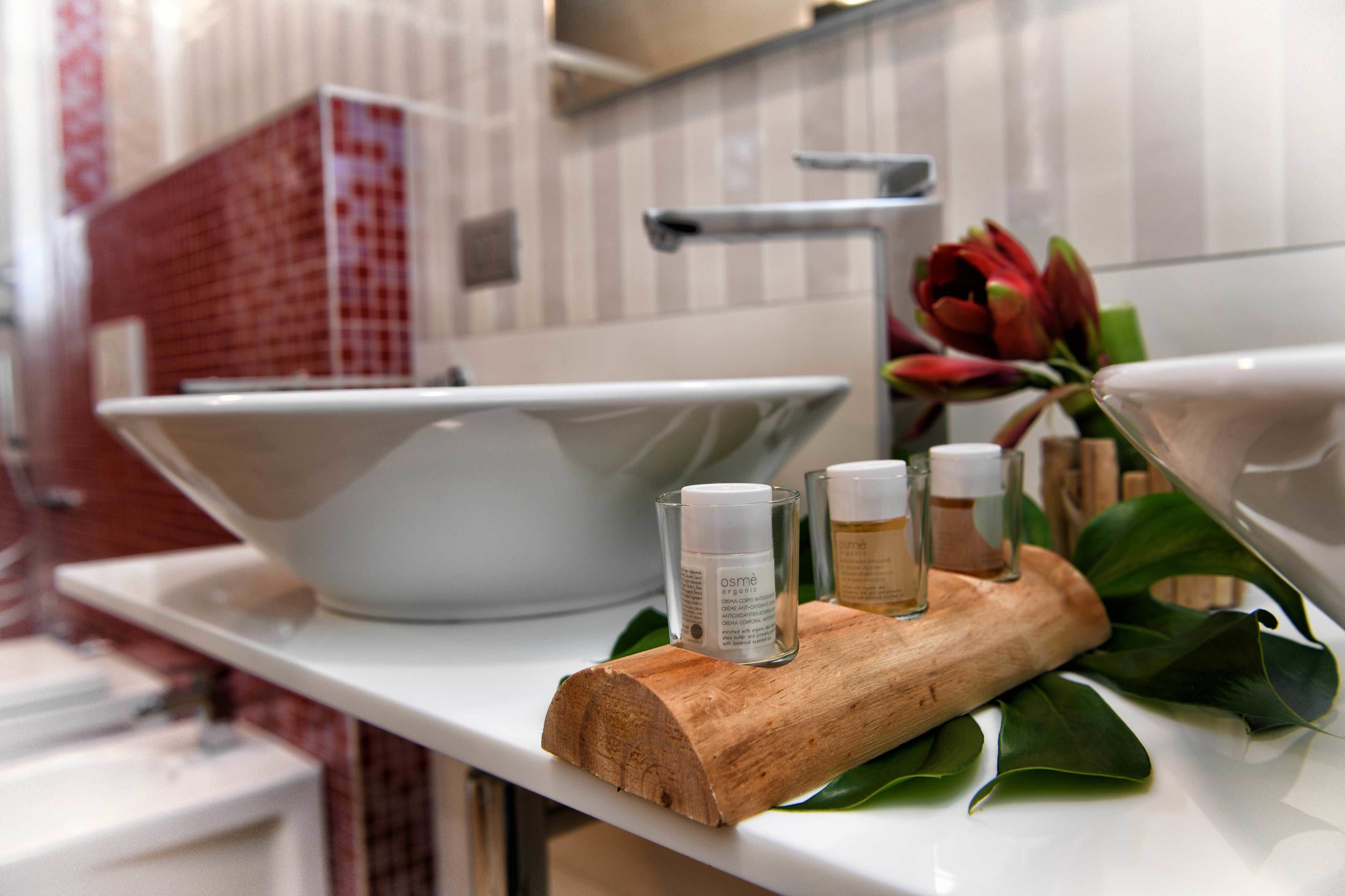 A bathroom vanity with a white sink, a wooden tray holding three bottles, and a red and white checkered towel.