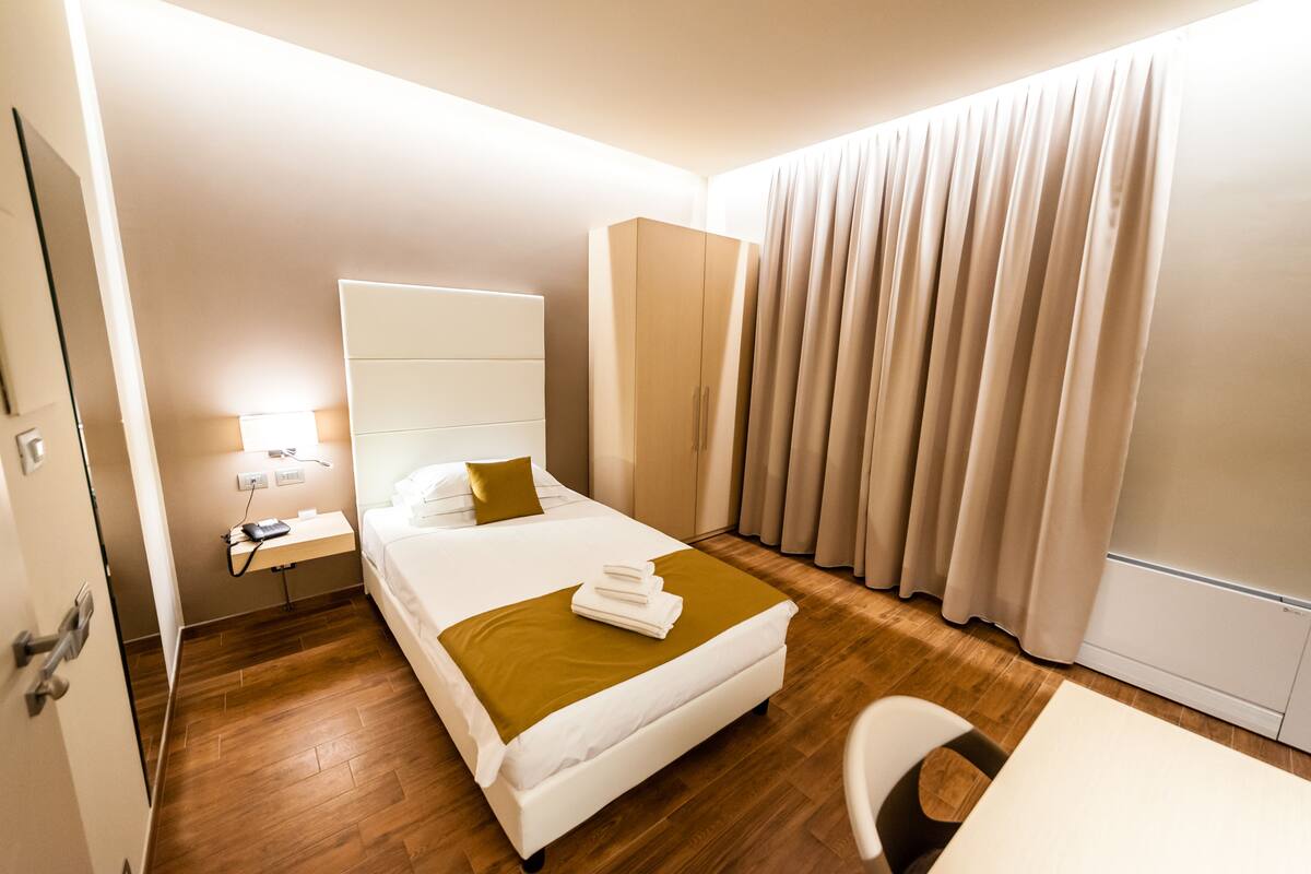 A hotel room with a bed, a desk, a chair, a wardrobe, and a window with curtains.