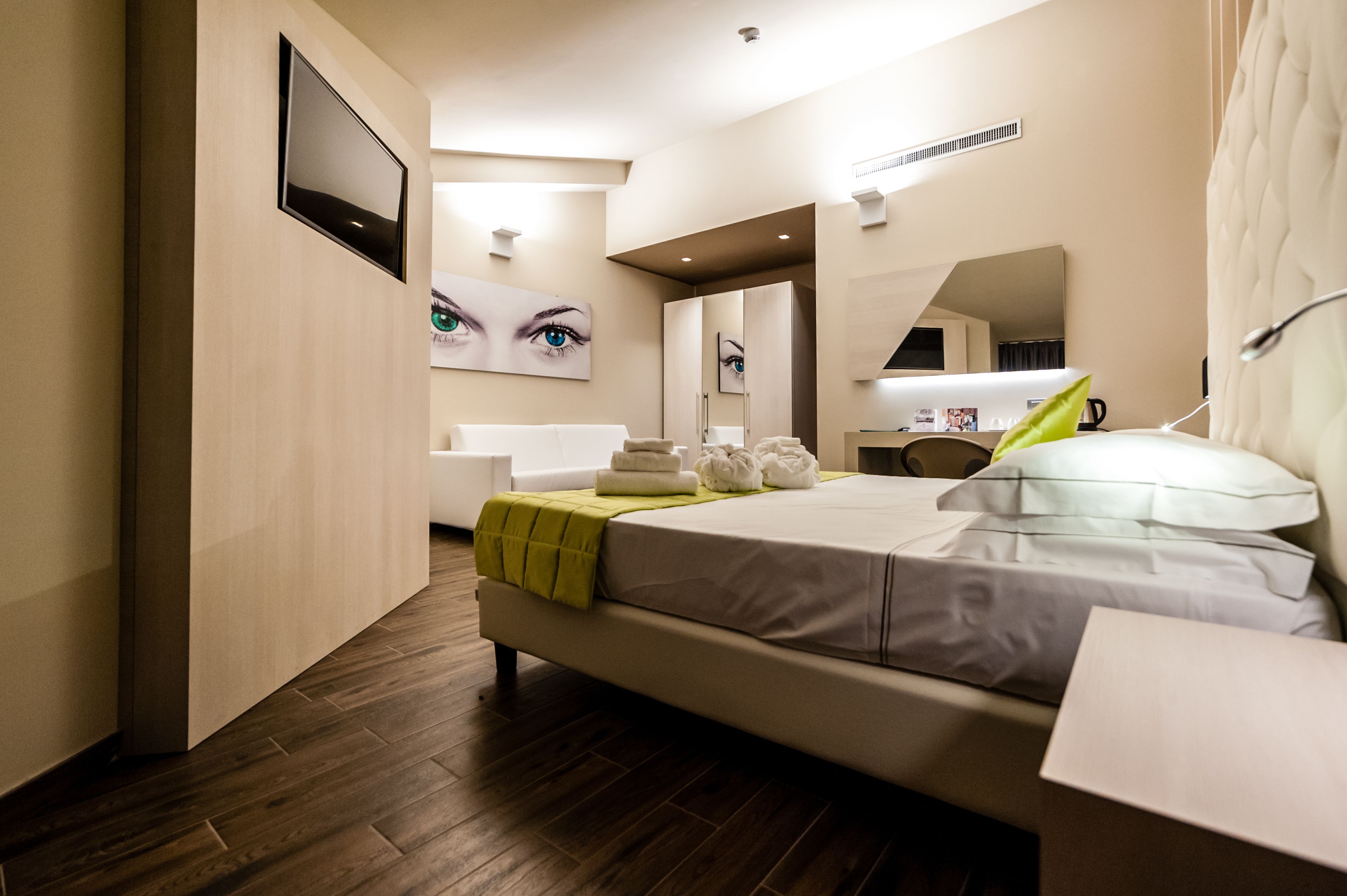 Habitación de hotel moderna con una cama grande, una mesita de noche, un espejo y un baño con bañera e inodoro.