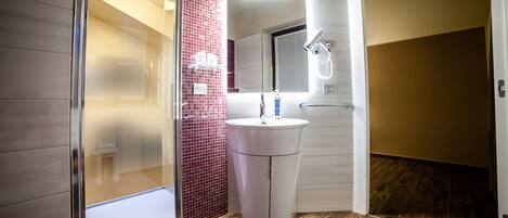 A modern bathroom with a glass shower enclosure, a white pedestal sink, and a mirror above it.