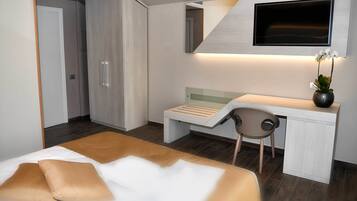 A modern hotel room with a bed, a desk, a chair, a TV, and a wardrobe.