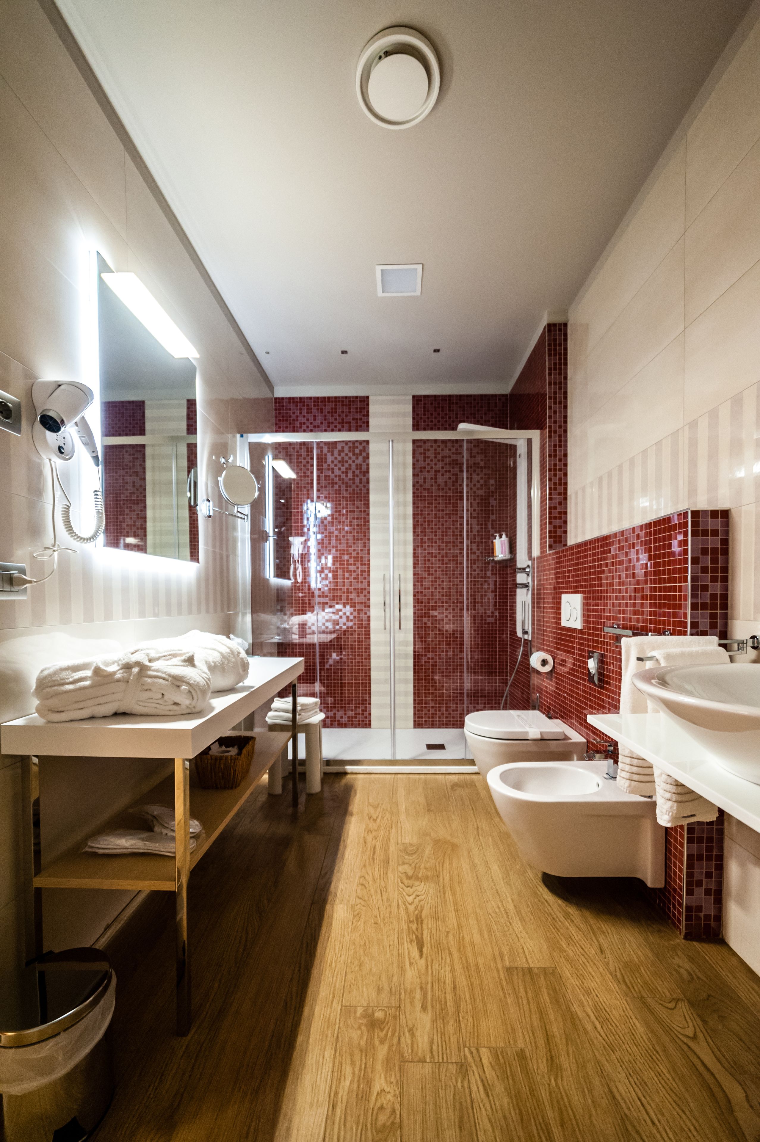Ein modernes Badezimmer mit Holzboden, zwei Waschbecken, einer Toilette und einer Duschkabine.