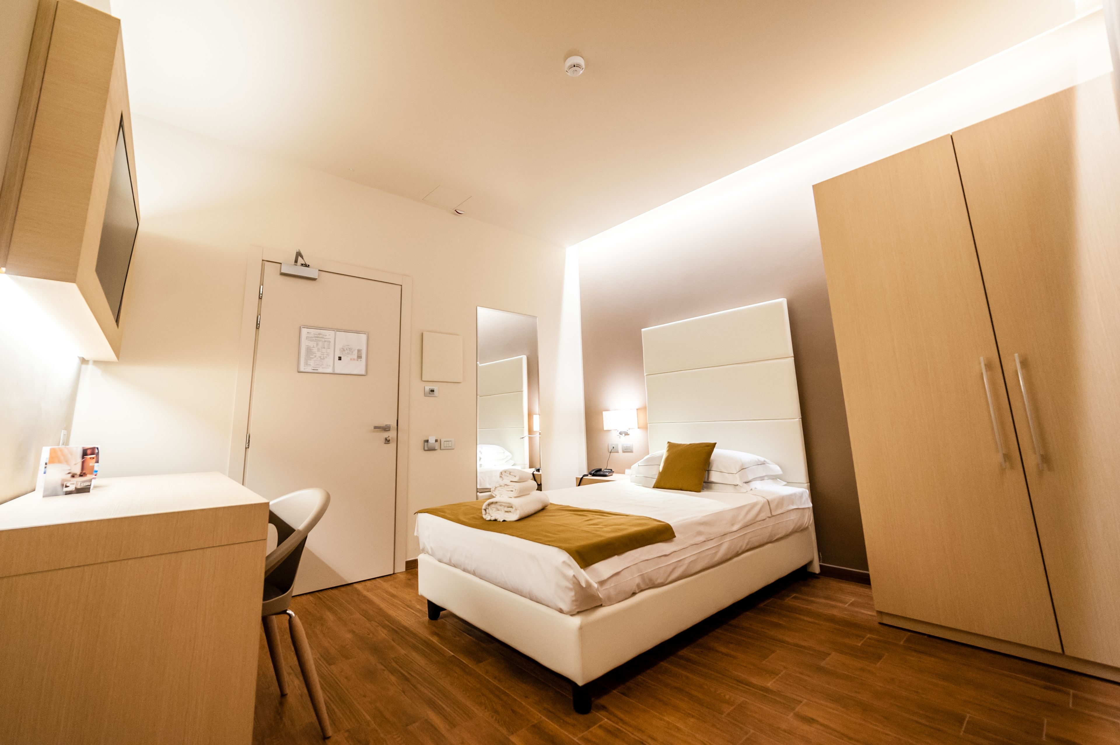 Une chambre d’hôtel comprenant un lit, une table de chevet, un bureau, une chaise, une armoire et un miroir.