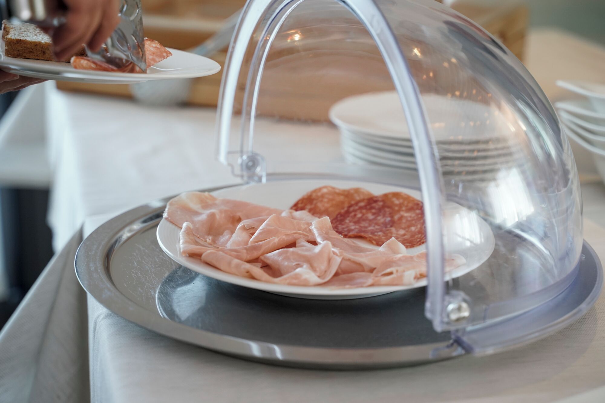 Una mesa de buffet con un plato de fiambres bajo una campana de cristal.