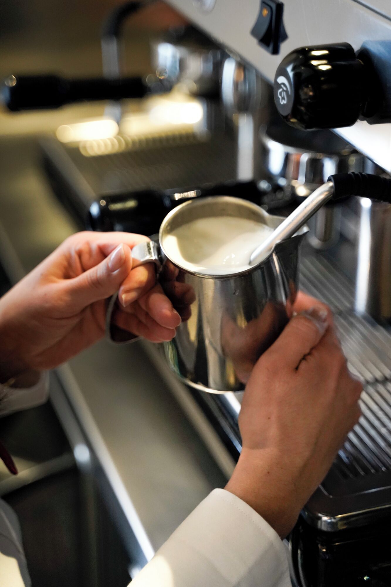 Una persona tiene una tazza di acciaio inossidabile sotto una macchina da caffè, probabilmente per preparare una bevanda.
