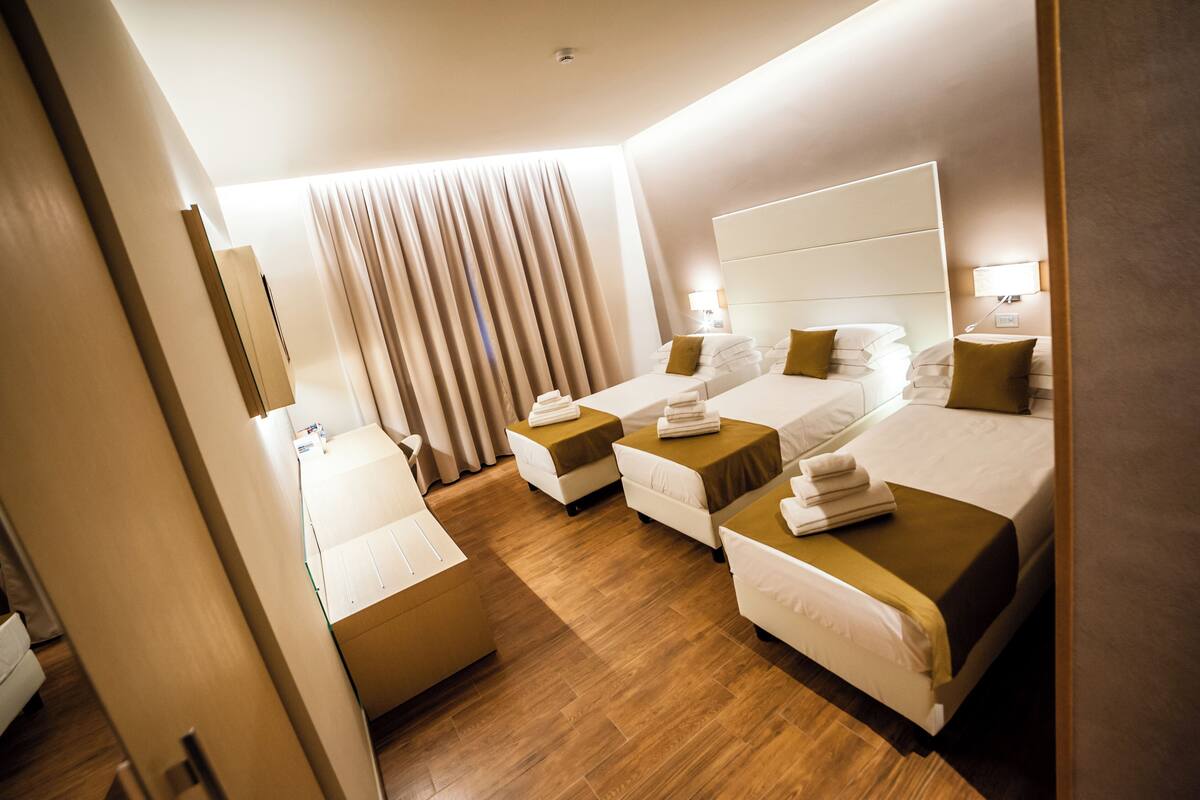A hotel room with three beds, a large window with curtains, and a wooden floor.