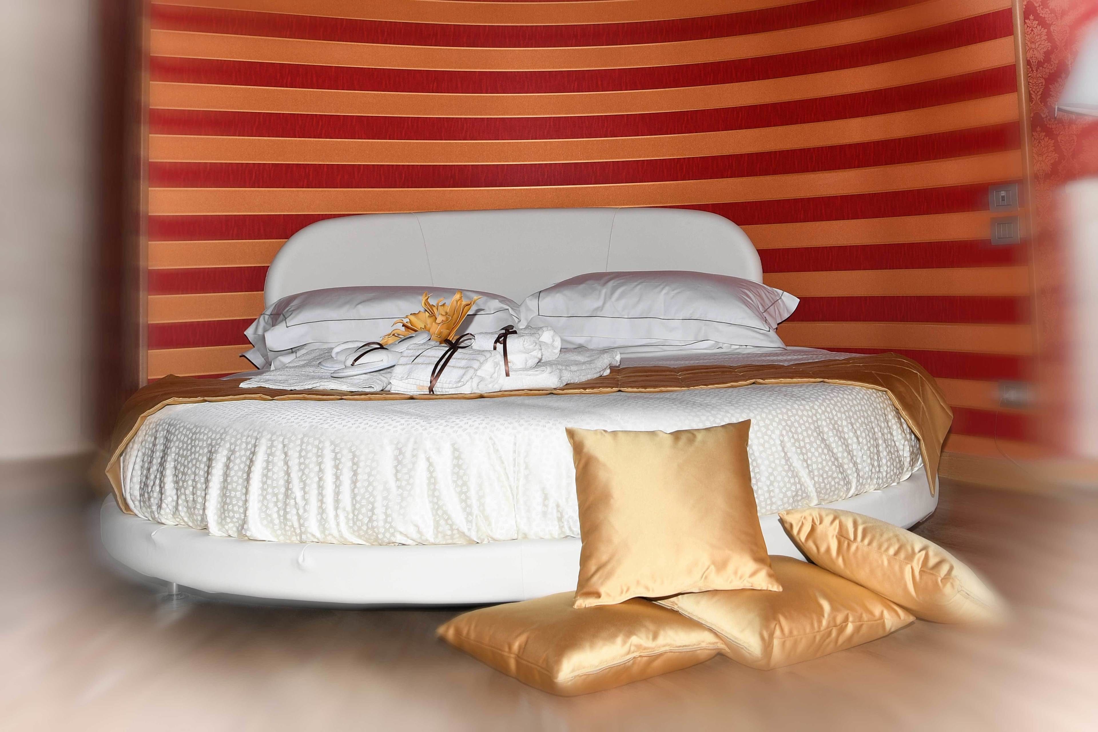 Ein Bett mit weißer Bettwäsche und goldenen Kissen, ein weißer Kopfseitenverzierer und eine Wand mit roten und orangefarbenen Streifen.