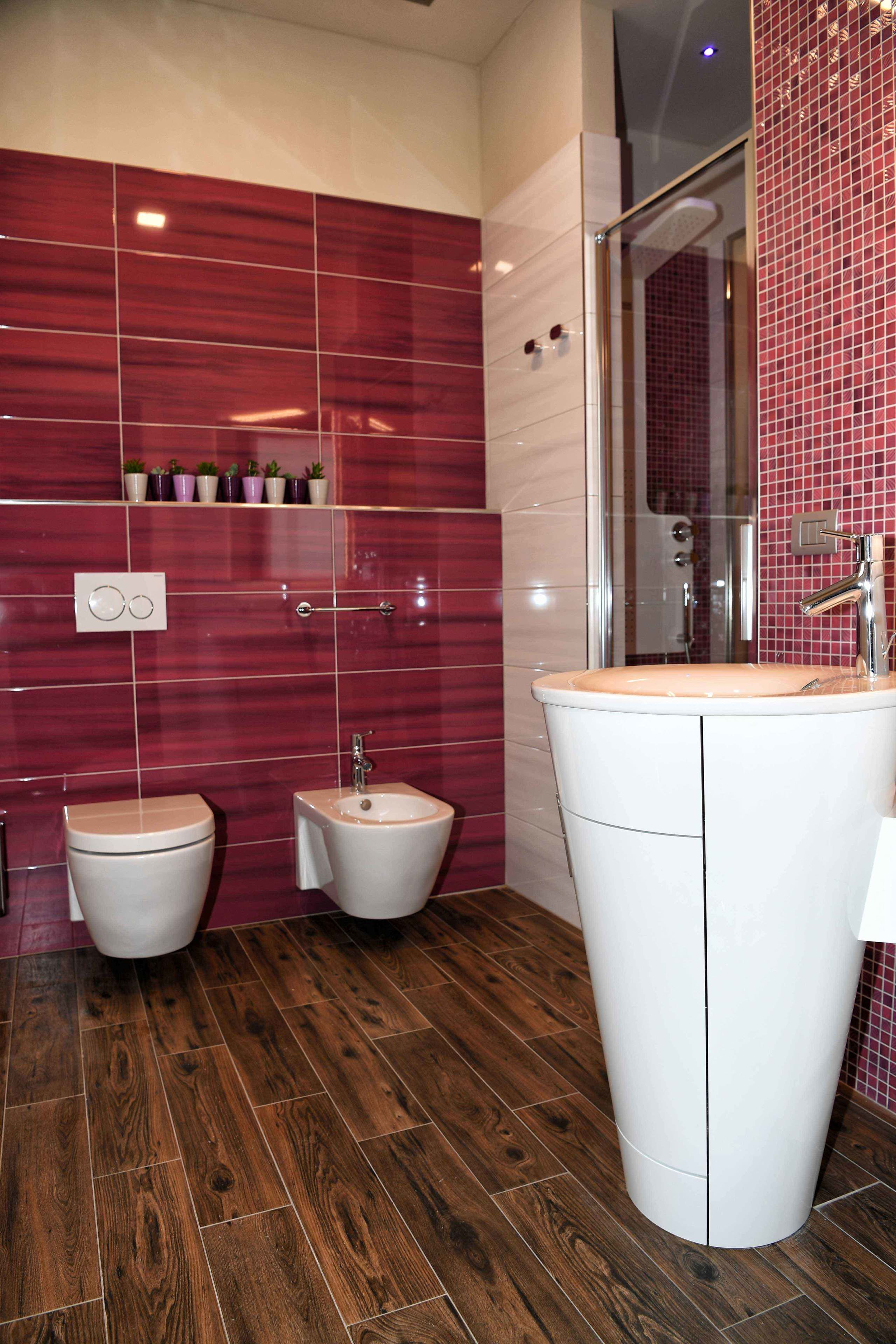 Une salle de bain avec un plancher en bois, un lavabo blanc et deux toilettes.