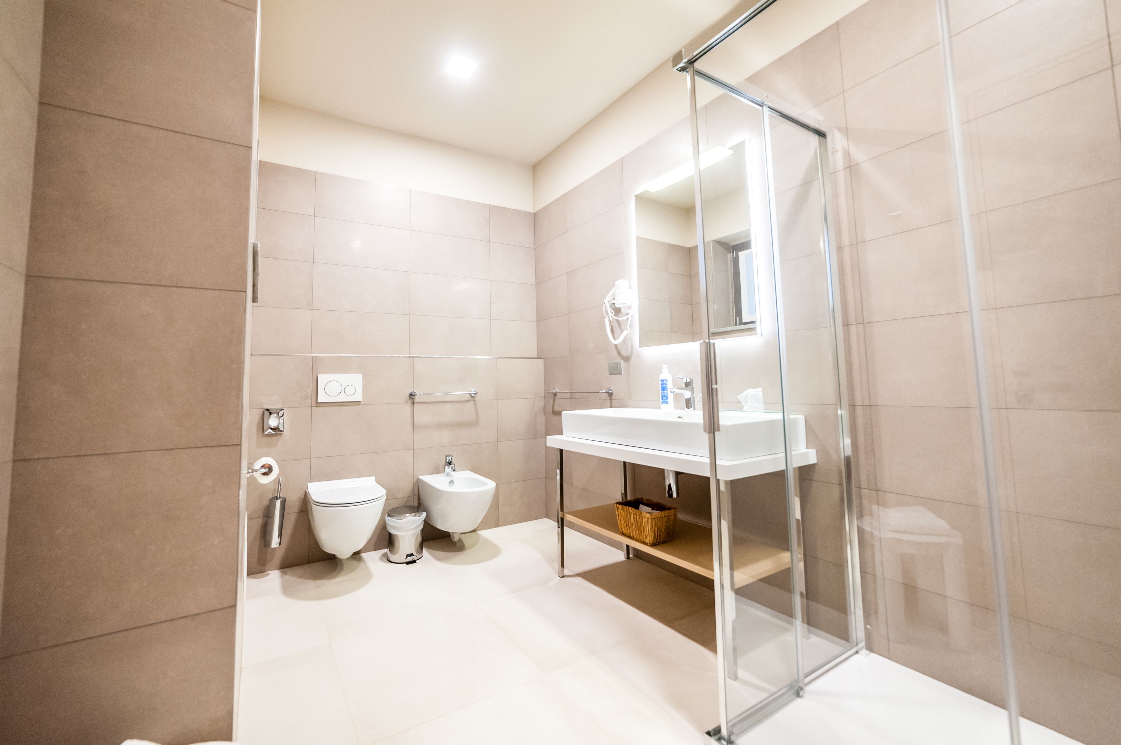 Un baño moderno con ducha de vidrio, lavamanos blanco y un bidé.