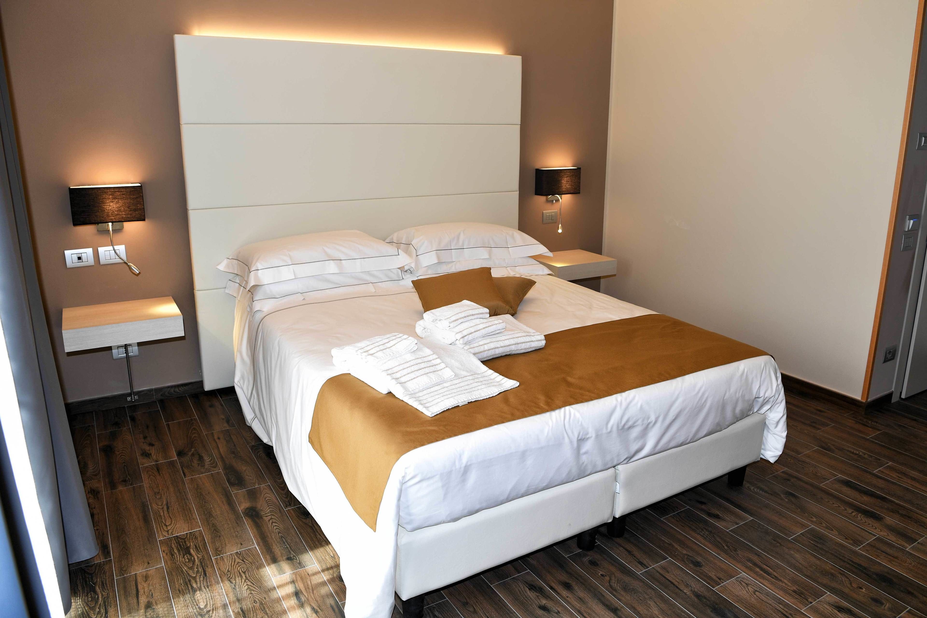 A modern hotel room with a large bed, two bedside tables, and wall-mounted lamps.
