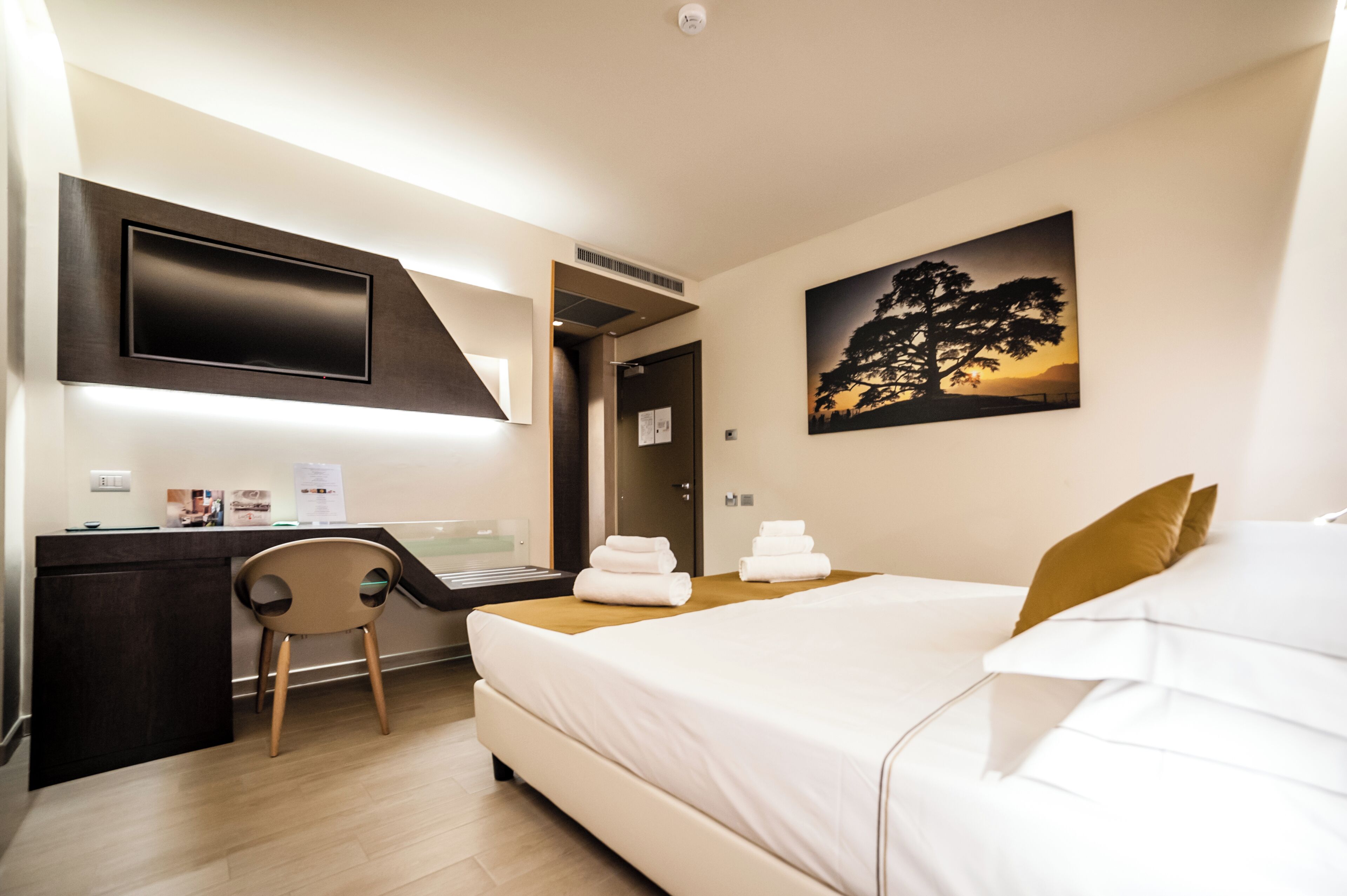 Una camera d'albergo con un letto, una scrivania, una sedia e un quadro appeso al muro.