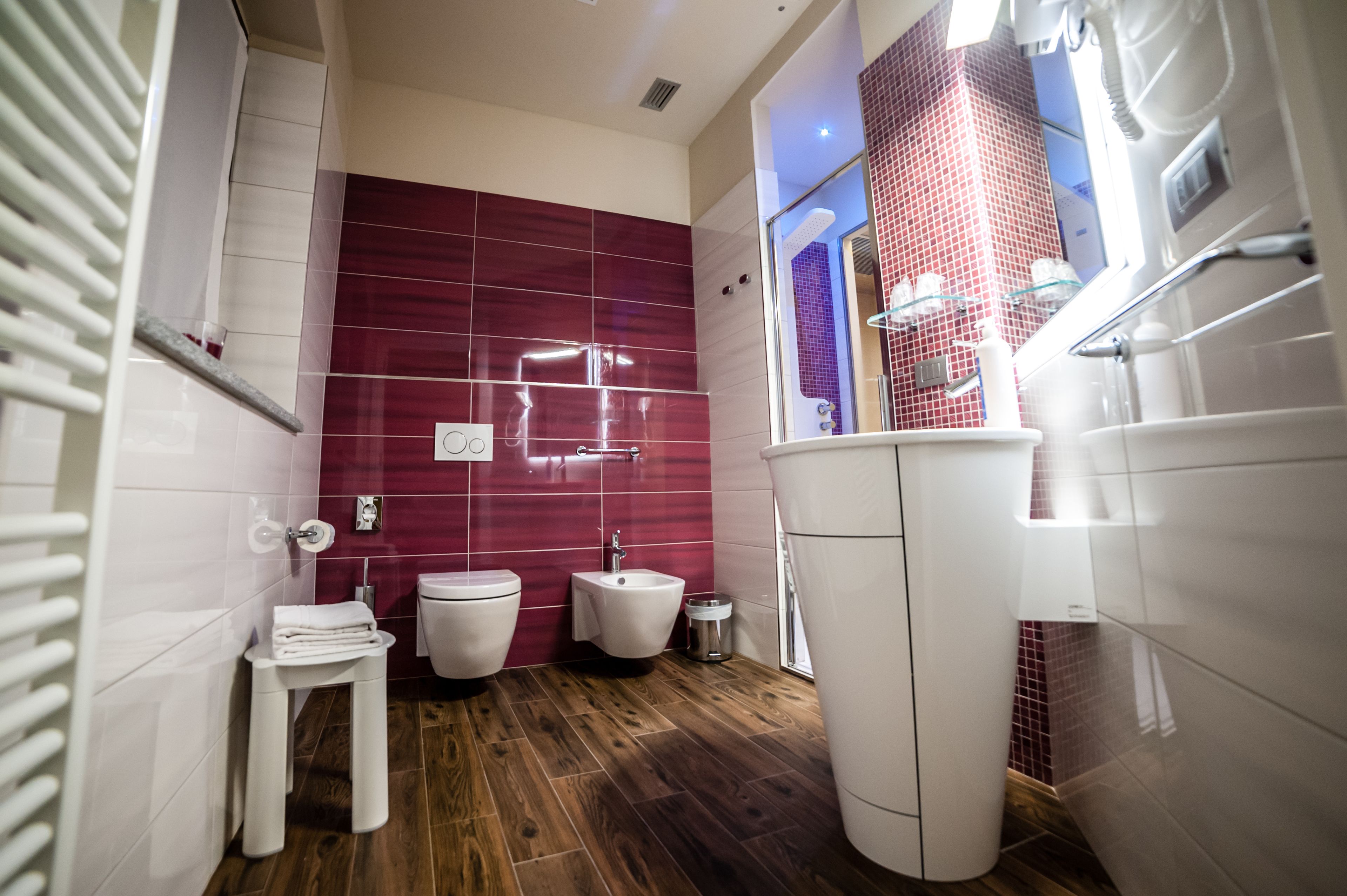 A modern bathroom with a wooden floor, white fixtures, and a red-tiled accent wall.