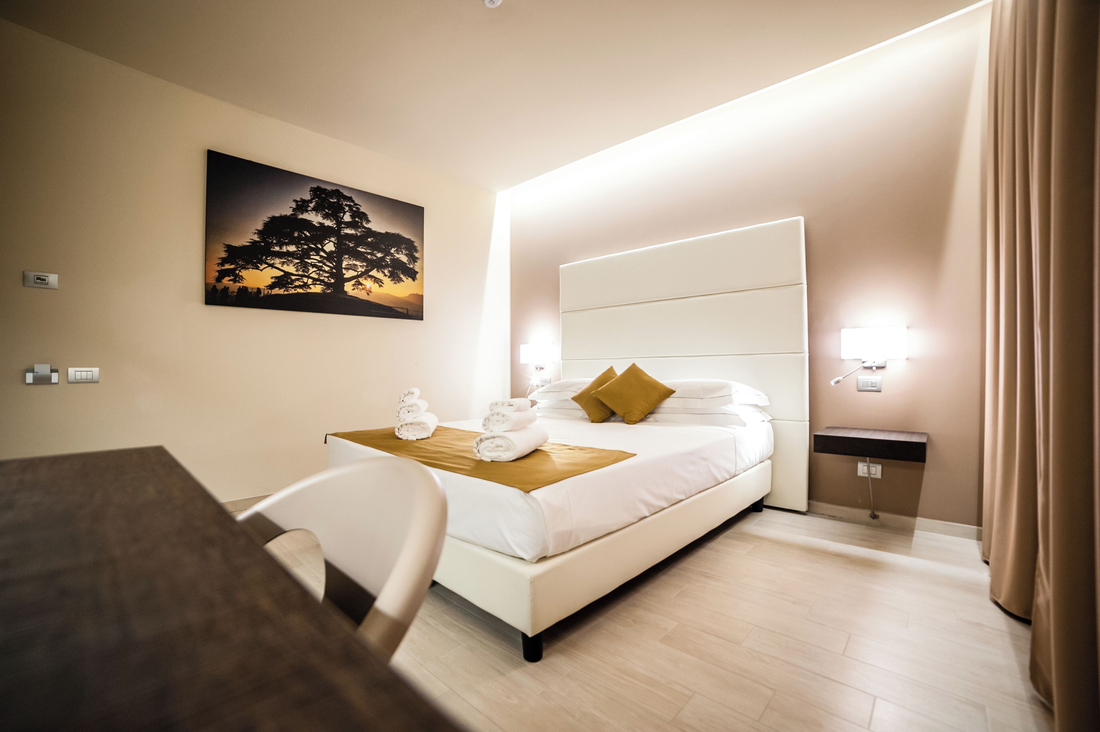 A hotel room with a bed, bedside table, and a painting on the wall.