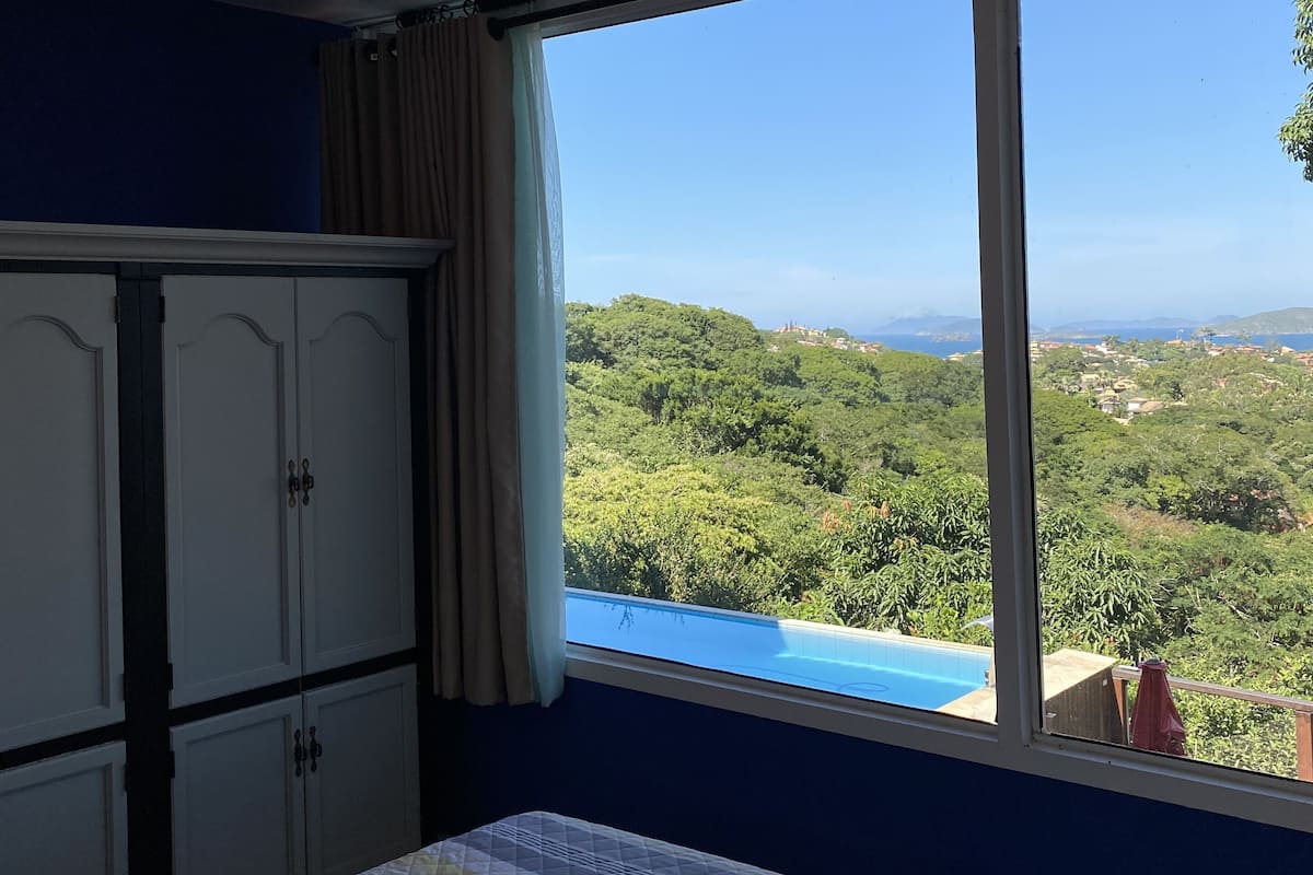 Une chambre à coucher comprenant un lit, un ventilateur de plafond, une armoire et une fenêtre donnant sur un paysage verdoyant.
