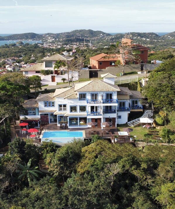 Una amplia casa de dos pisos con piscina, rodeada de vegetación exuberante y colinas al fondo.