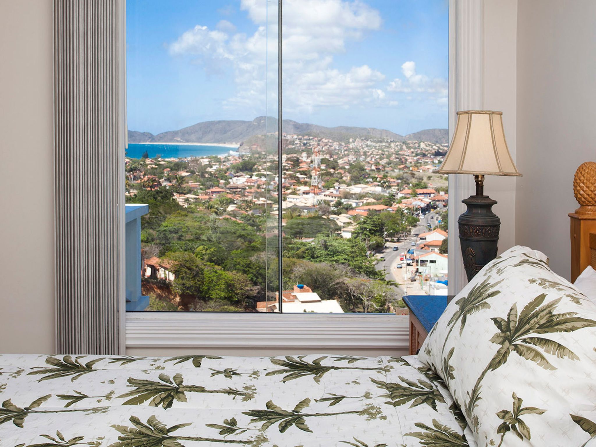 Quarto com uma grande janela que oferece vista para uma cidade costeira e montanhas.