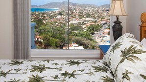 A bedroom with a large window offering a view of a coastal town and mountains. - Top de Buzios Boutique (Búzios)