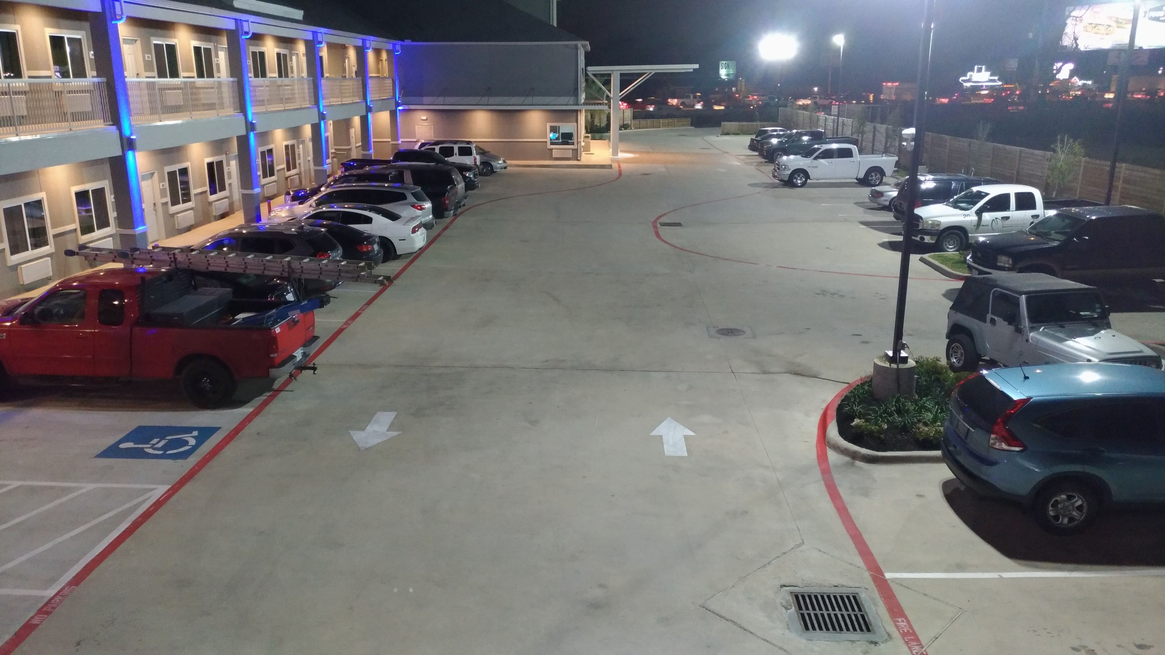 A parking lot with multiple cars, a handicap parking space, and a building with blue lighting.